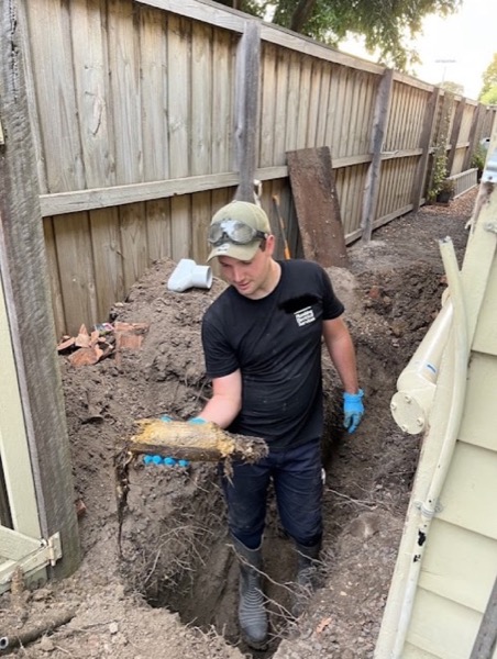 A Fast Fix plumber in an excavated trench holding a section of pipe packed solid with roots
